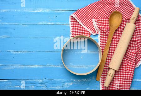 Wooden rolling pin, round wooden sieve on blue background with red napkin Stock Photo