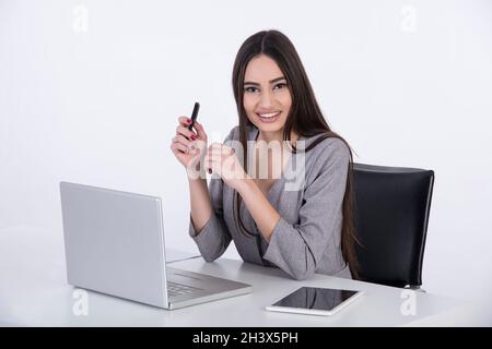 Young business woman with black hair siiting at her office on white backround and working on a computer. Stock Photo