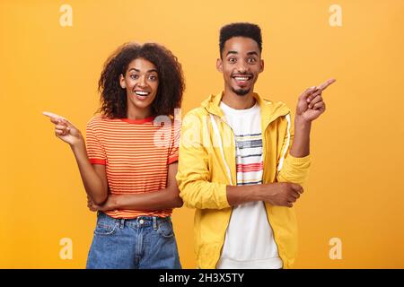 Which one telling true. Joyful and friendly good-looking couple, african american woman pointing left and dark-skinned guy right Stock Photo