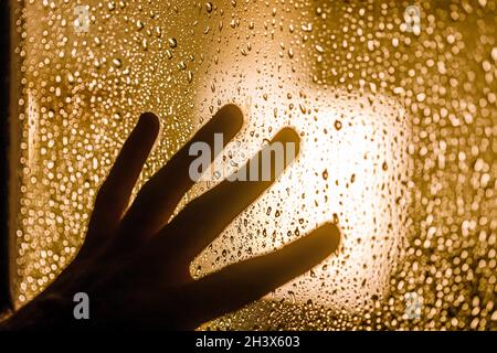 Depression and goodbye concept: dark silhouette of human hand on window with rain drops Stock Photo
