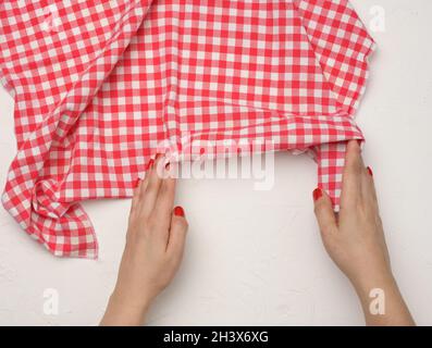 Two female hands hold a crumpled white-red checkered textile kitchen napkin on a white table Stock Photo