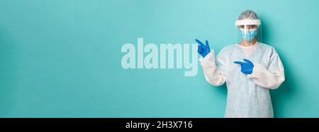 Concept of covid-19, pandemic and health. Confident female doctor in personal protective equipment, pointing fingers left at cop Stock Photo