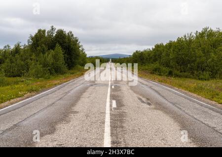 Endless gravel road leading trhough forest and tundra wilderness in a straight line to the horizon Stock Photo