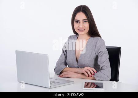 Asian business woman sitting at her office in front of her computer and tablet. She is wearing a grey suit. Stock Photo