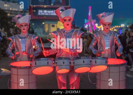 30th Oct, 2021. Southend on Sea, UK. Three performers in metallic silver costumes and elaborate headpieces play glowing red drums during a night-time street performance at the Southend Halloween Parade 2025. The scene captures the vibrant energy of the event, with theatrical makeup, illuminated instruments, and a festive crowd lining the seafront. A double-decker bus and colourful lights add to the urban spectacle. Penelope Barritt/Ģ����ý Live News Stock Photo