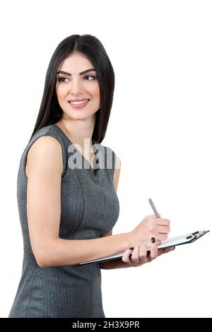 Young woman wearing a gray dress and holding a note pad and taking notes. She is looking away and smiling. Stock Photo
