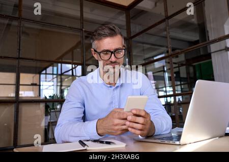 Caucasian businessman holding in hands using smartphone in office with laptop. Stock Photo