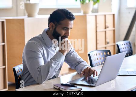 Concentrated Indian ceo businessman working in modern office using laptop. Stock Photo
