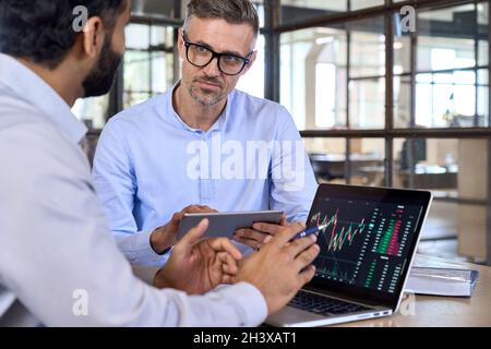 Diverse businessmen traders discussing cryptocurrency at desk using devices. Stock Photo