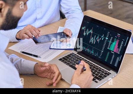 Two traders using laptop and tablet with cryptocurrencies graphs. Closeup. Stock Photo