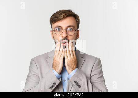 Close-up of startled businessman in gray suit and glasses, gasping and looking surprised, standing over white background Stock Photo