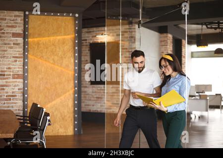Two young focused coworkers, woman and man, looking through documents from folderwalking in office Stock Photo