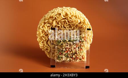 Circle of instant noodles with raw spices on a plain brown background. Sprinkle dry Chinese or Korean vermicelli with salt and s Stock Photo