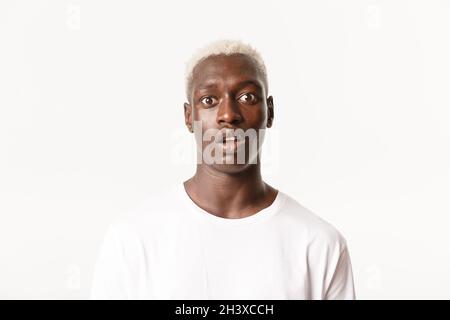 Close-up of startled gasping african-american blond man, drop jaw and looking wondered at camera, standing white background Stock Photo