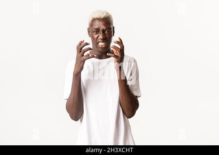 Portrait of angry african-american blond man, clenching hands and looking hateful, feeling outraged or bothered, standing over w Stock Photo