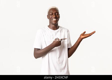 Portrait of smiling proud african-american man pointing at hand, holding something, standing white background Stock Photo