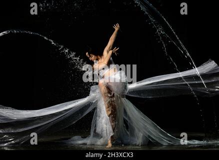 Young beautiful woman of Caucasian appearance with long hair dances in drops of water on a black background Stock Photo