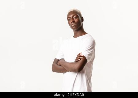 Portrait of confident assertive african-american guy with blond hair, cross arms chest and looking sassy, standing white backgro Stock Photo
