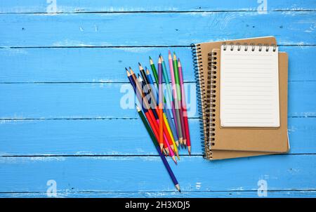 Multicolored wooden pencils, blank spiral notepads on blue table Stock Photo
