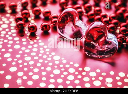 Shining transparent hearts and a group of red beads. Perfect Valentine's Day greeting card background. Vertical image in red ton Stock Photo