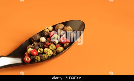 A mixture of hot, red, black, white and green peppers in a black spoon. Isolated on a brown background. Stock Photo