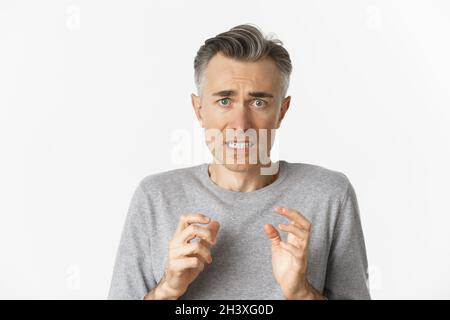 Close-up of anxious middle-aged man, looking scared and nervous, feeling guilty, standing over white background Stock Photo