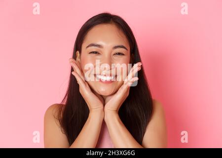 Beauty, fashion and lifestyle concept. Close-up of beautiful asian girl touching her face and smiling silly, blushing, feeling r Stock Photo