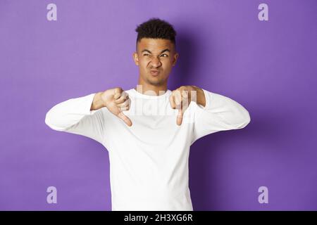 Image of skeptical and disappointed african-american young man, looking at something disgusting at upper left corner, showing th Stock Photo