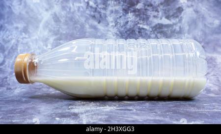 A semi-empty plastic bottle of fresh regular milk lies on a dark gray marble or concrete backdrop. Close-up front view. World mi Stock Photo