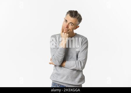Portrait of bored and unamused middle-aged man in grey sweater, leaning on hand and looking at camera reluctant, standing sad ov Stock Photo