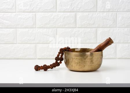 Tibetan singing copper bowl with a wooden clapper on a white wooden table, objects for meditation and alternative medicine Stock Photo
