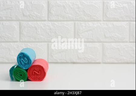 Stack of disposable plastic trash can bags on white table, white brick wall background Stock Photo