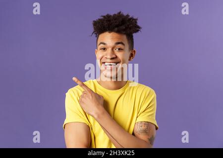 Close-up portrait of cheerful, attractive young male student showing promo, pointing at upper left corner, smiling pleased, reco Stock Photo