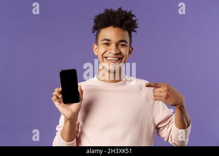 Close-up portrait of young handsome man promoting smartphone app or shopping online, internet delivery for goods, holding mobile Stock Photo