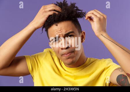 Close-up portrait of grimacing young focused guy looking in mirror at his haircut, need call his stylish or hairdresser, making Stock Photo