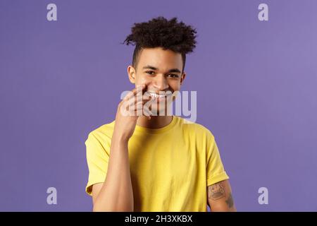 Close-up portrait of lovely young hispanic gay man with dreads, tattoos, touching lip sensually and flirty smiling, checking out Stock Photo