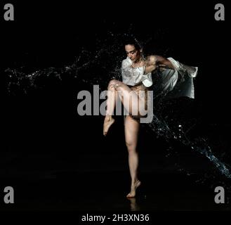 Young beautiful woman of Caucasian appearance with long black hair is dancing in a white shirt in the rain on a black background Stock Photo