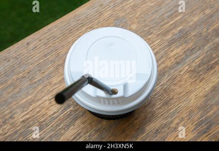 One black paper coffee cup with lid outdoors in summer in sunny weather on a wooden table of a cafe, coffee shop or restaurant. Stock Photo