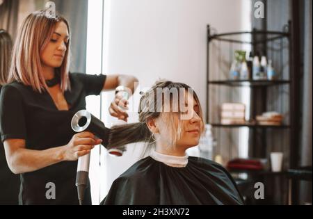 Happy woman with stylist making hairdo at salon Stock Photo