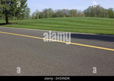 Asphalt road for cyclists and pedestrians through the green lawn in the park. A walk in the spring park. Stock Photo