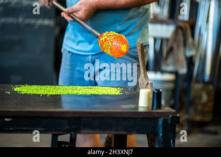 a worker is in the process of creating a glass vase and is rolling glass and adding decoration during the process of glass blowing Stock Photo