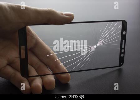 Broken protective glass of smartphone with cracks in hand on black background. Stock Photo