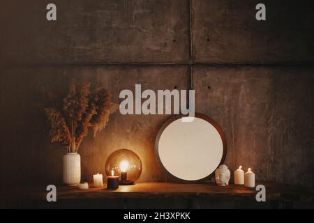 Round mirror on wooden shelf with two burning candles and small porcelain Buddha head Stock Photo