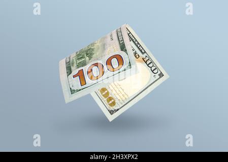 A bent one hundred dollar bill falls in free fall and casts a shadow against a blue background, stgflation or inflation concept. Stock Photo