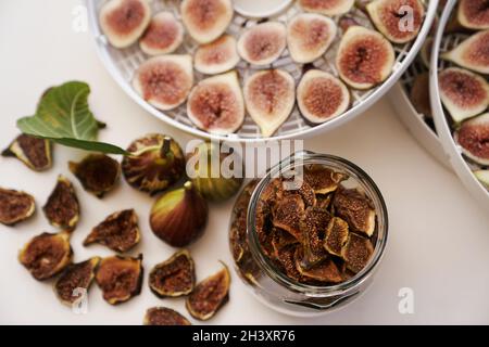 Fresh figs lie on the table next to dried figs in a glass jar and a dehydrator. Top view Stock Photo