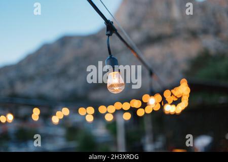 A garland of incandescent light bulbs, in the evening, against the backdrop of bokeh. Stock Photo