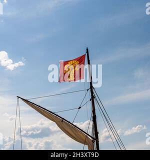 Flag of the Finnish city of Vaasa flying in a strong wind from the mast of an old sailboat under a blue sky Stock Photo