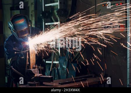 Man in mask cuts metal with plasma cutter. Helmet and spakrs Stock Photo