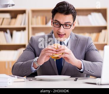 Hungry funny businessman eating junk food sandwich Stock Photo