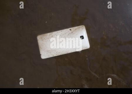 Mobile phone lying on pavement in puddle. Stock Photo